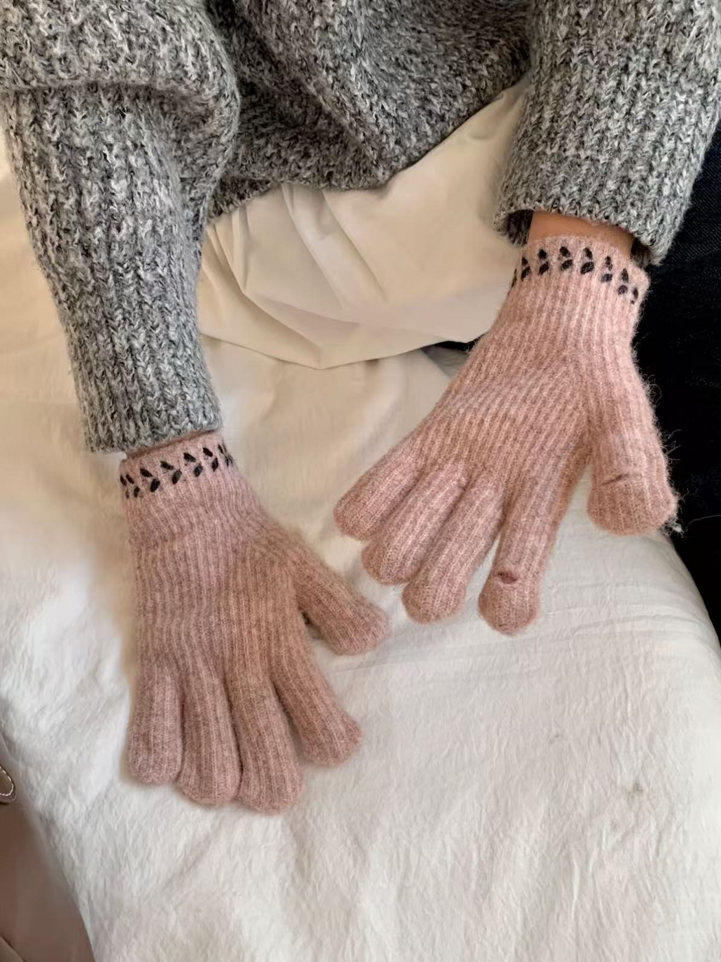 Ribbed gloves with dark cuff embroidery, hands resting on a white seat