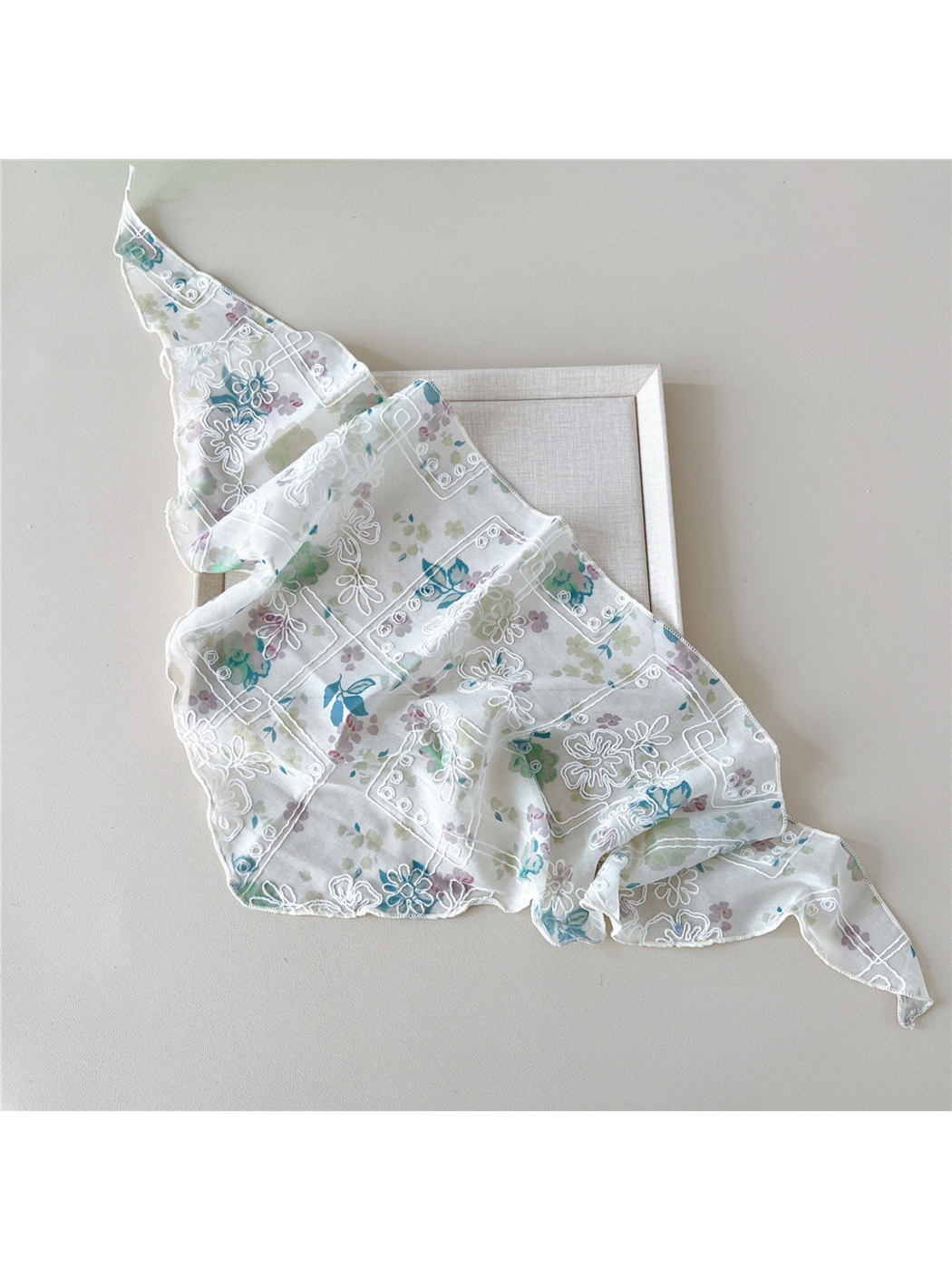 Floral scarf with white embroidery loosely spread diagonally over a tray