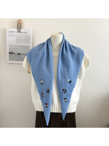 Sky Blue knit scarf draped open over a white top, showing embroidered figures on both ends