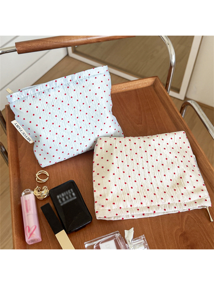 Blue cosmetic pouch standing beside an Ivory pouch lying flat, both with small red polka dots