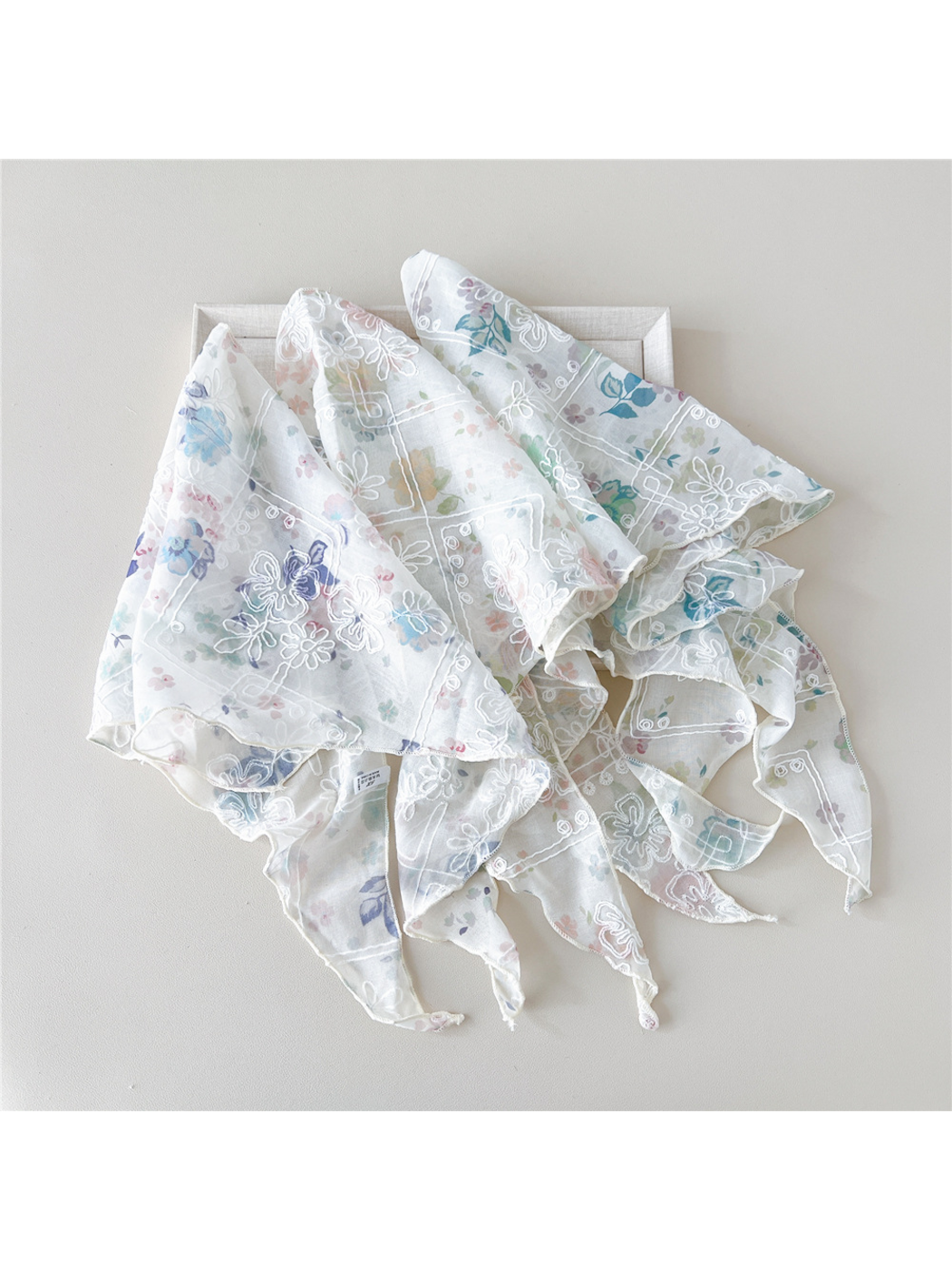 Floral scarves with white embroidery loosely gathered across a tray