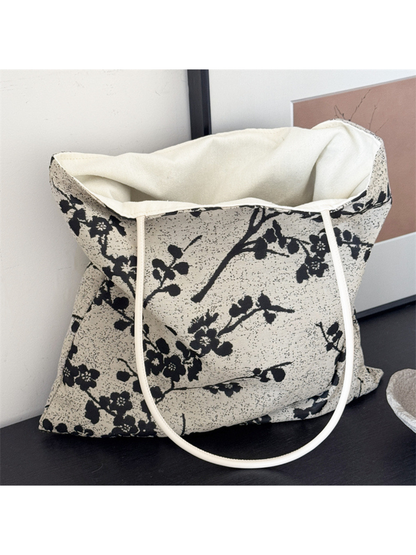 Black flowering-branch tote bag standing open with ivory lining and loop handles