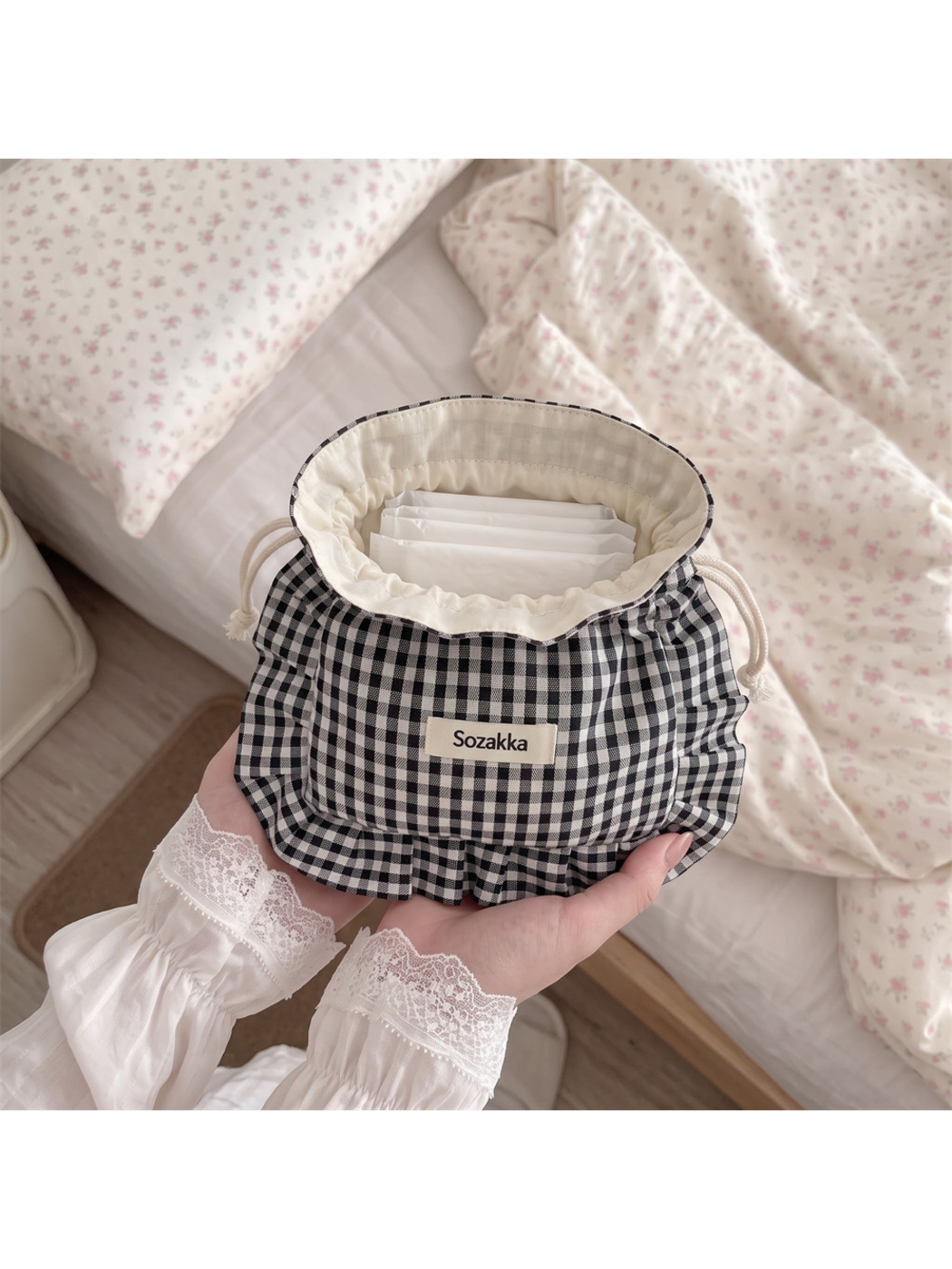 Black gingham drawstring pouch held open, showing the cream lining and white packets