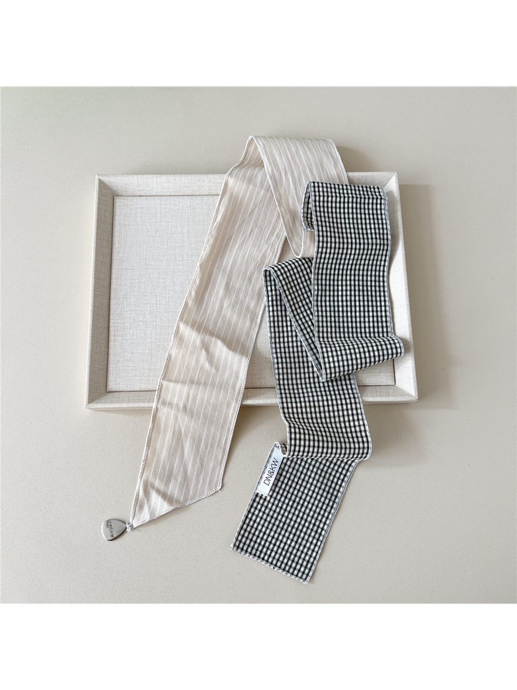 Beige scarf draped untied with narrow white stripes, black and white gingham checks and a teardrop charm