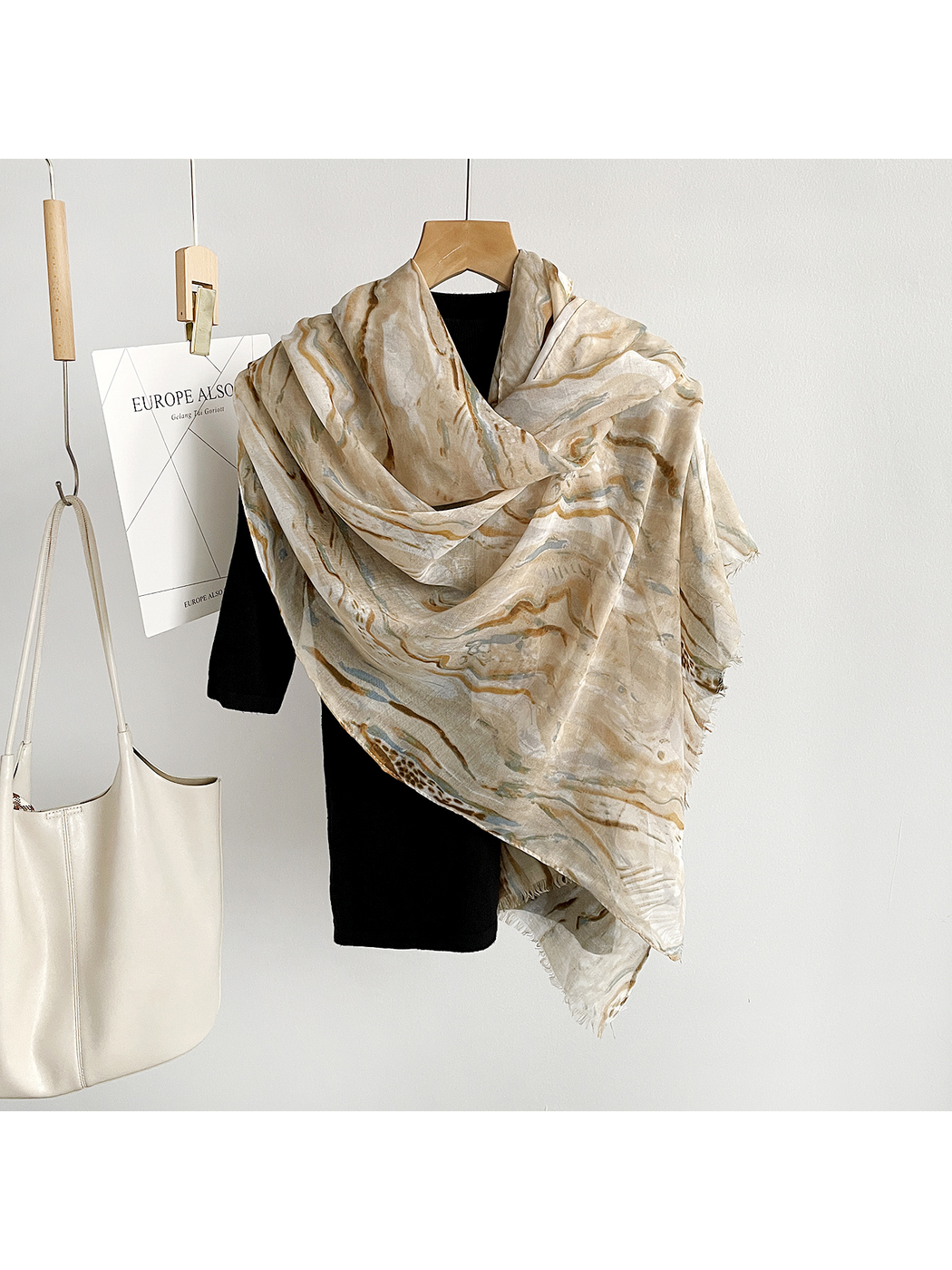 Beige marbled scarf draped broadly over a black top with fringed ends