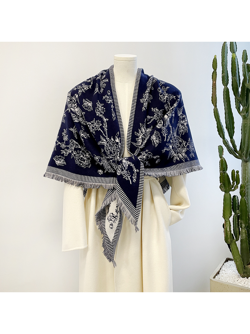 Navy floral scarf tied over a cream coat on a mannequin