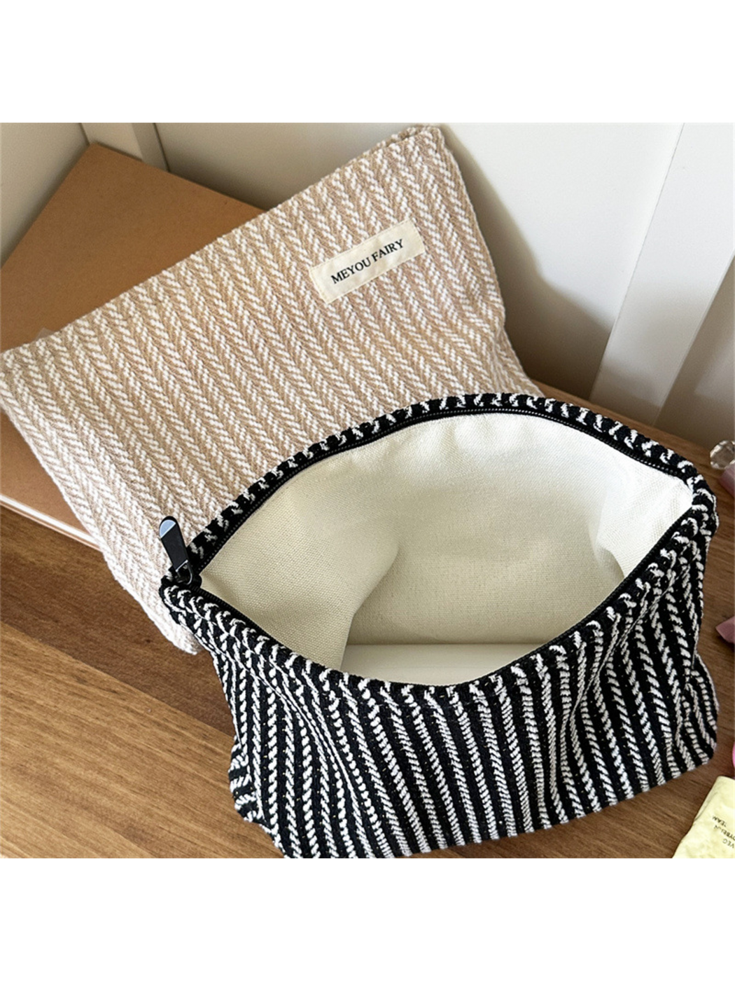 Open Black makeup pouch showing its empty pale interior, with Beige pouch behind
