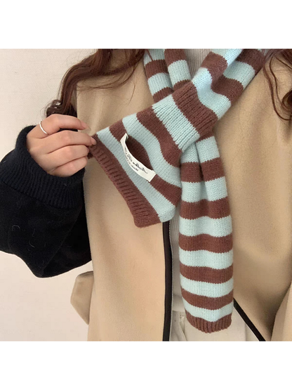 Mint striped knit scarf worn over a beige vest, with one ribbed end held outward