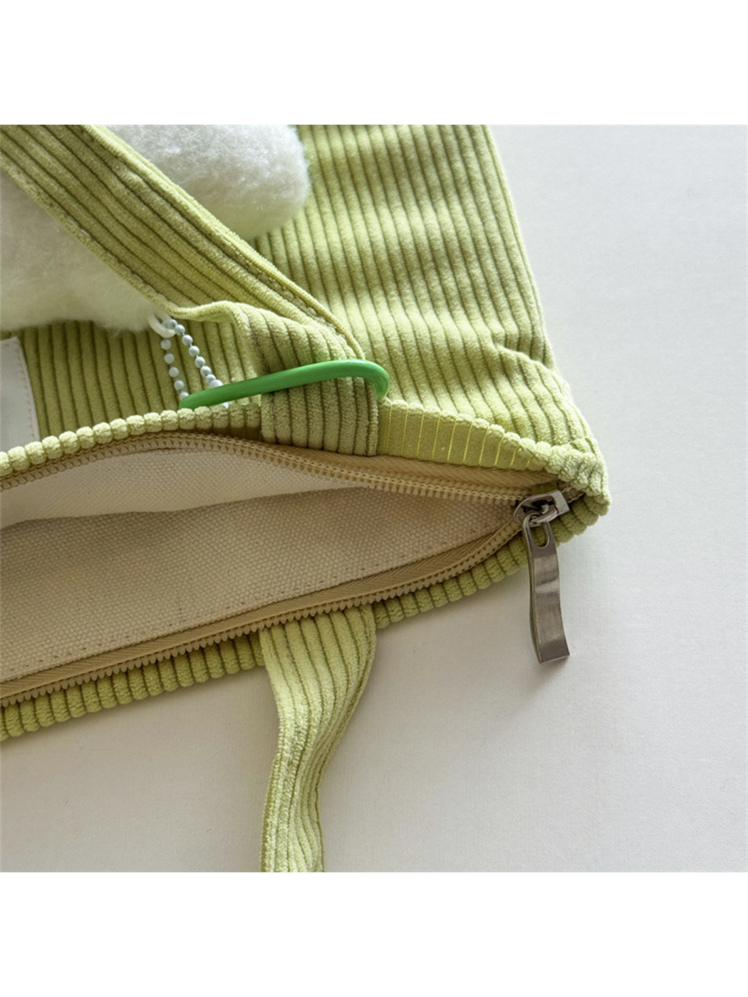 Close-up of Green tote bag top edge, silver-colored pull and handle attachment