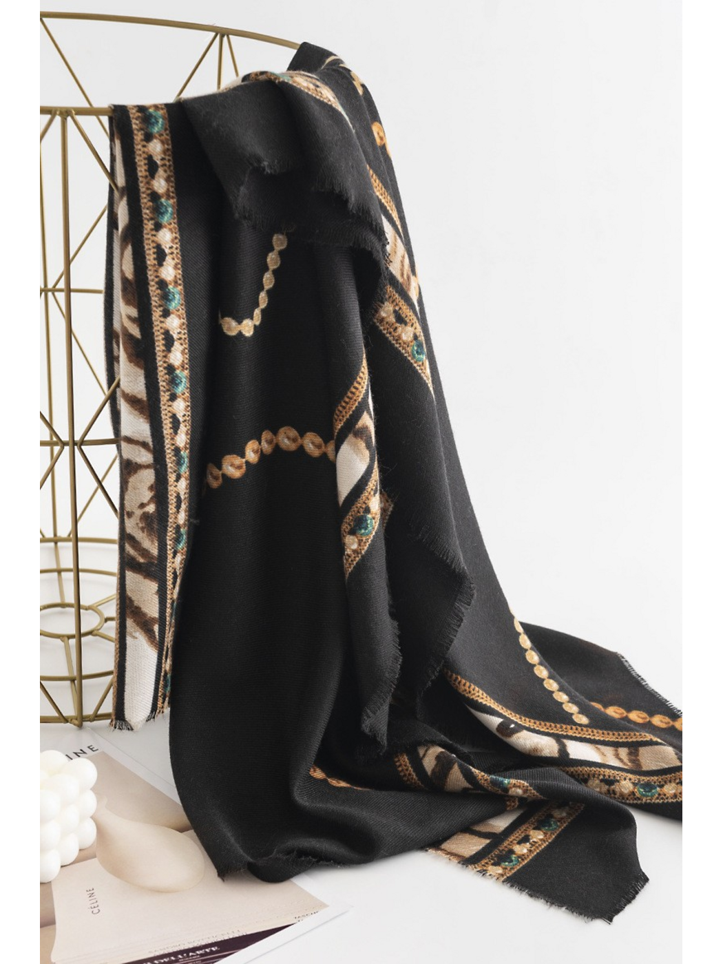 Black scarf draped over a gold-tone stand, showing its ornamental border and hanging folds