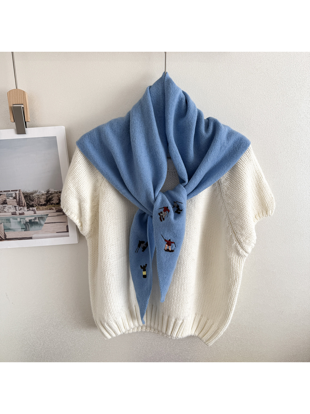 Sky Blue embroidered knit scarf looped over a hanging white top
