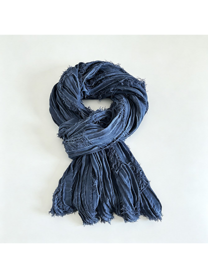 Blue textured scarf looped on a pale background with fringed ends spread below