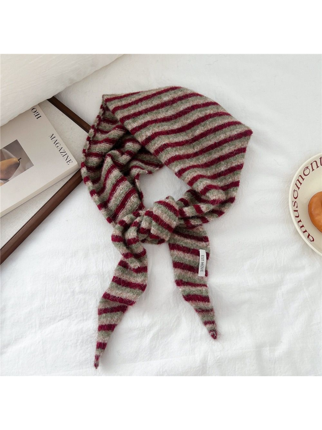 Striped fuzzy scarf looped and tied on white fabric beside a magazine