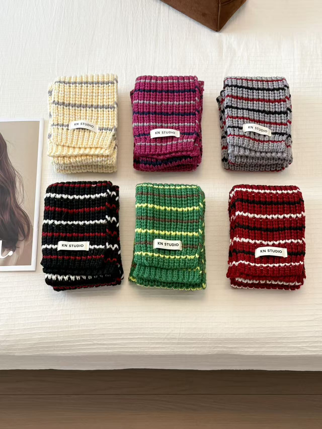 Beige, Fuchsia, Gray, Black, Green and Burgundy striped knit scarves folded in two rows