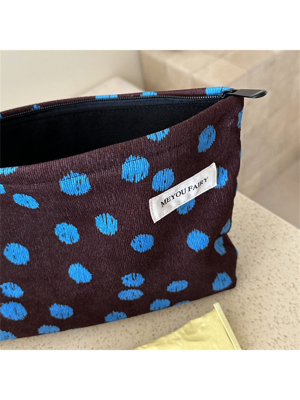 Close-up of the Brown cosmetic bag's blue dots, ribbed surface and white label