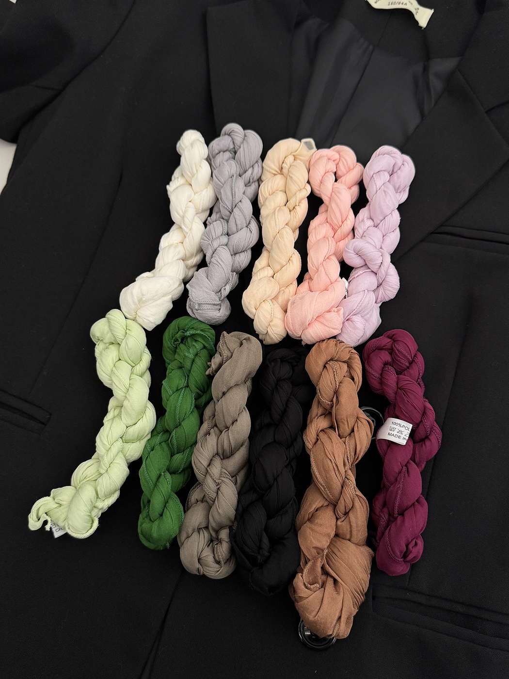 Eleven crinkled scarves twisted into compact bundles on a black jacket