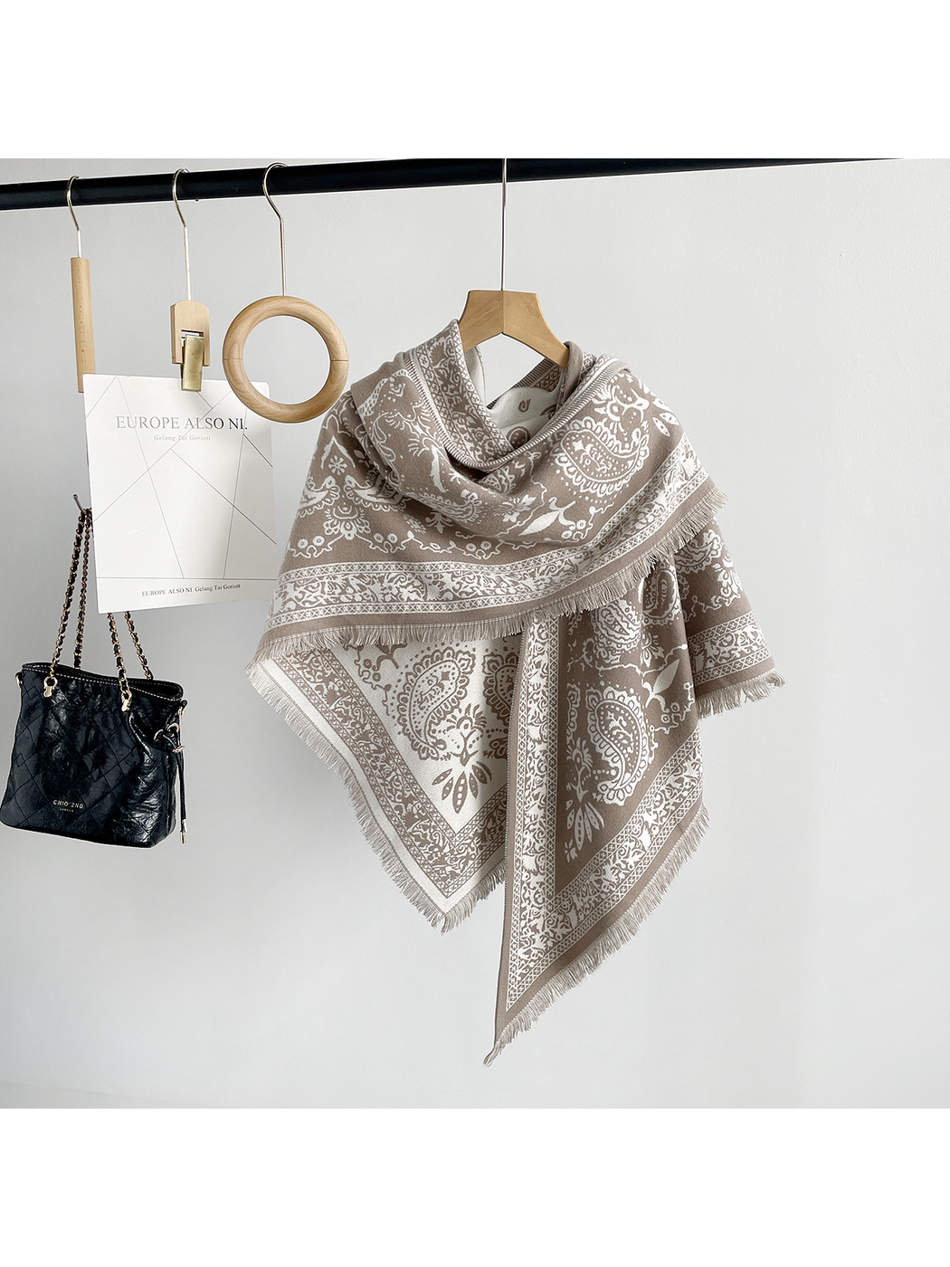 Khaki paisley scarf draped on a hanger with ivory motifs, ornamental borders and fringe