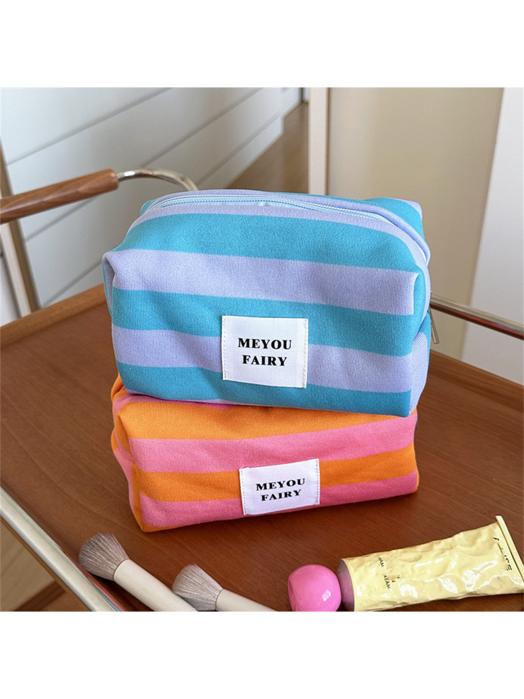 Turquoise striped makeup bag stacked above an Orange striped bag