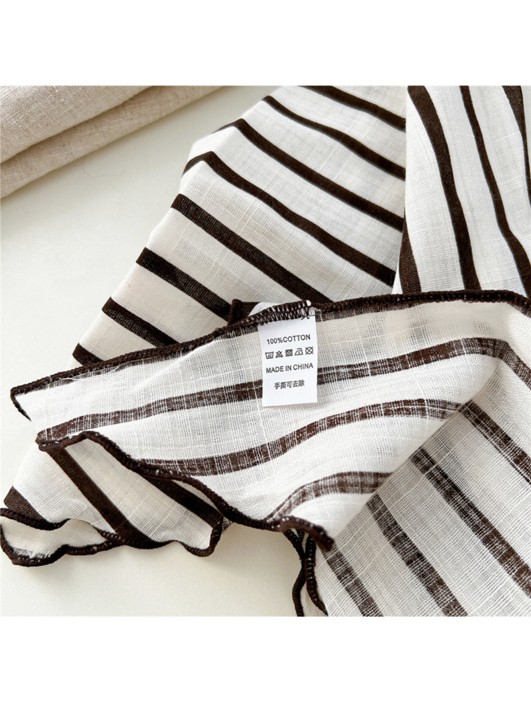 Close-up of an ivory striped scarf showing woven texture, dark edge stitching and attached label