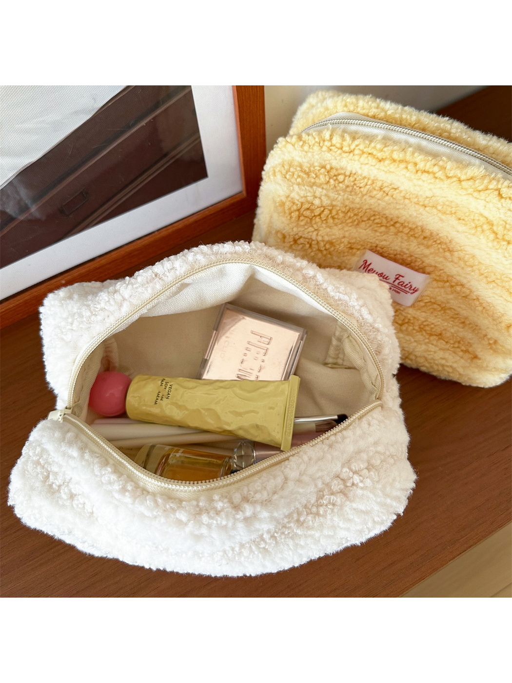 Open Ivory cosmetic pouch showing light-colored lining and styled cosmetics, with a partially visible Yellow pouch behind