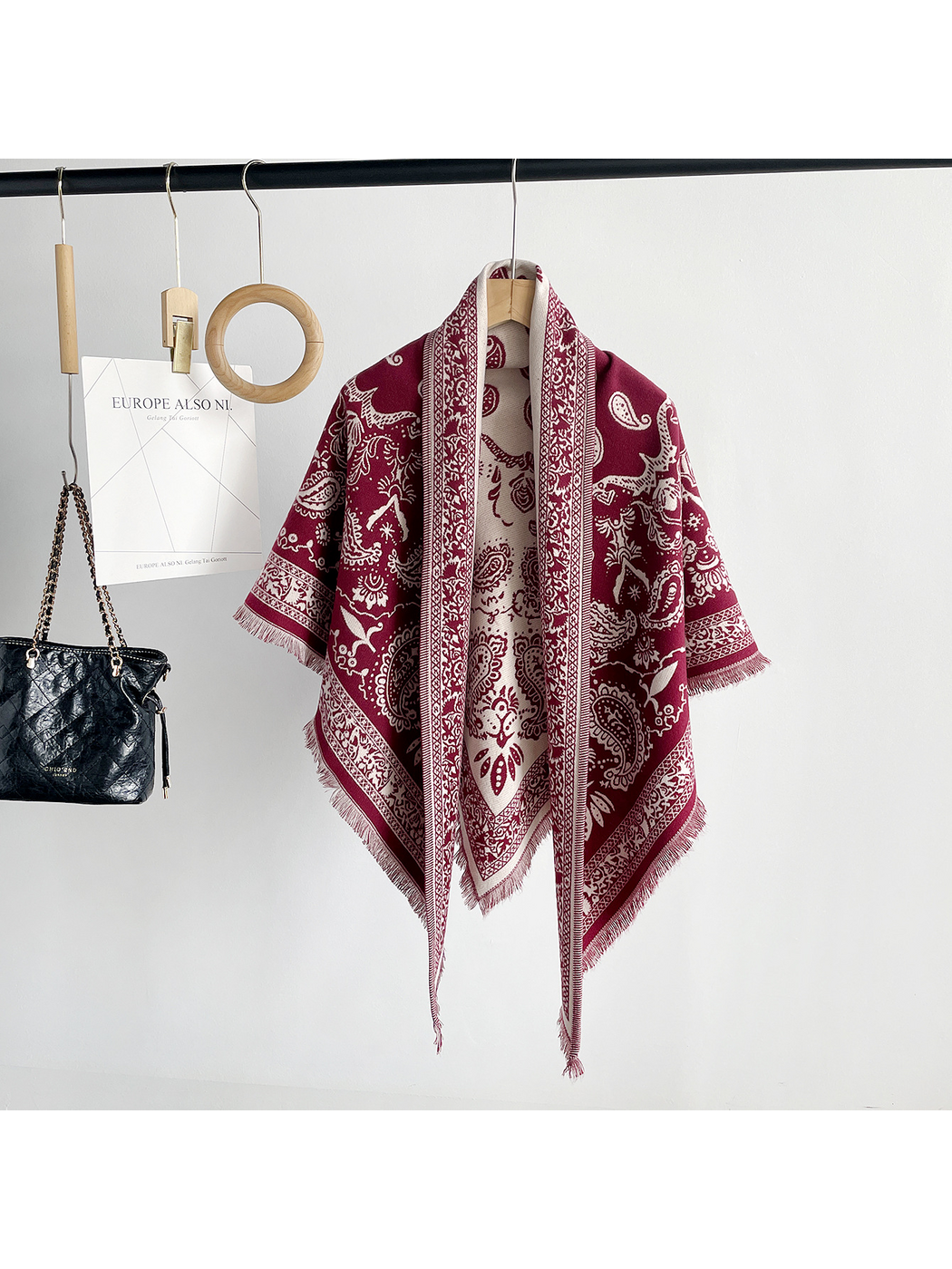 Black paisley scarf draped on a hanger with ivory ornamental borders and fringe