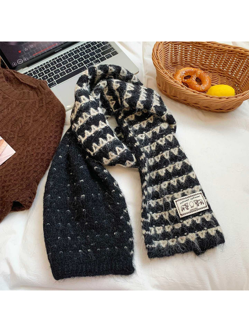 Black knit scarf draped on bedding, showing ivory zigzag bands and a dotted reverse