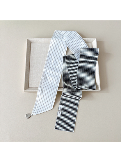 White scarf draped untied, showing striped and gingham sections, contrasting ends and a teardrop charm