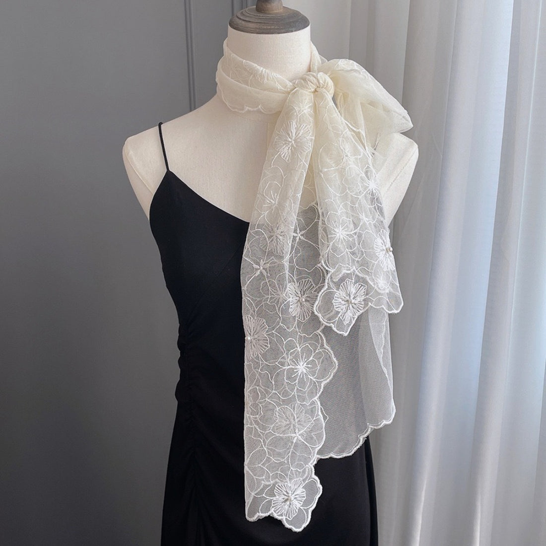 Woman tying floral lace scarf with pearl trim around her neck outdoors