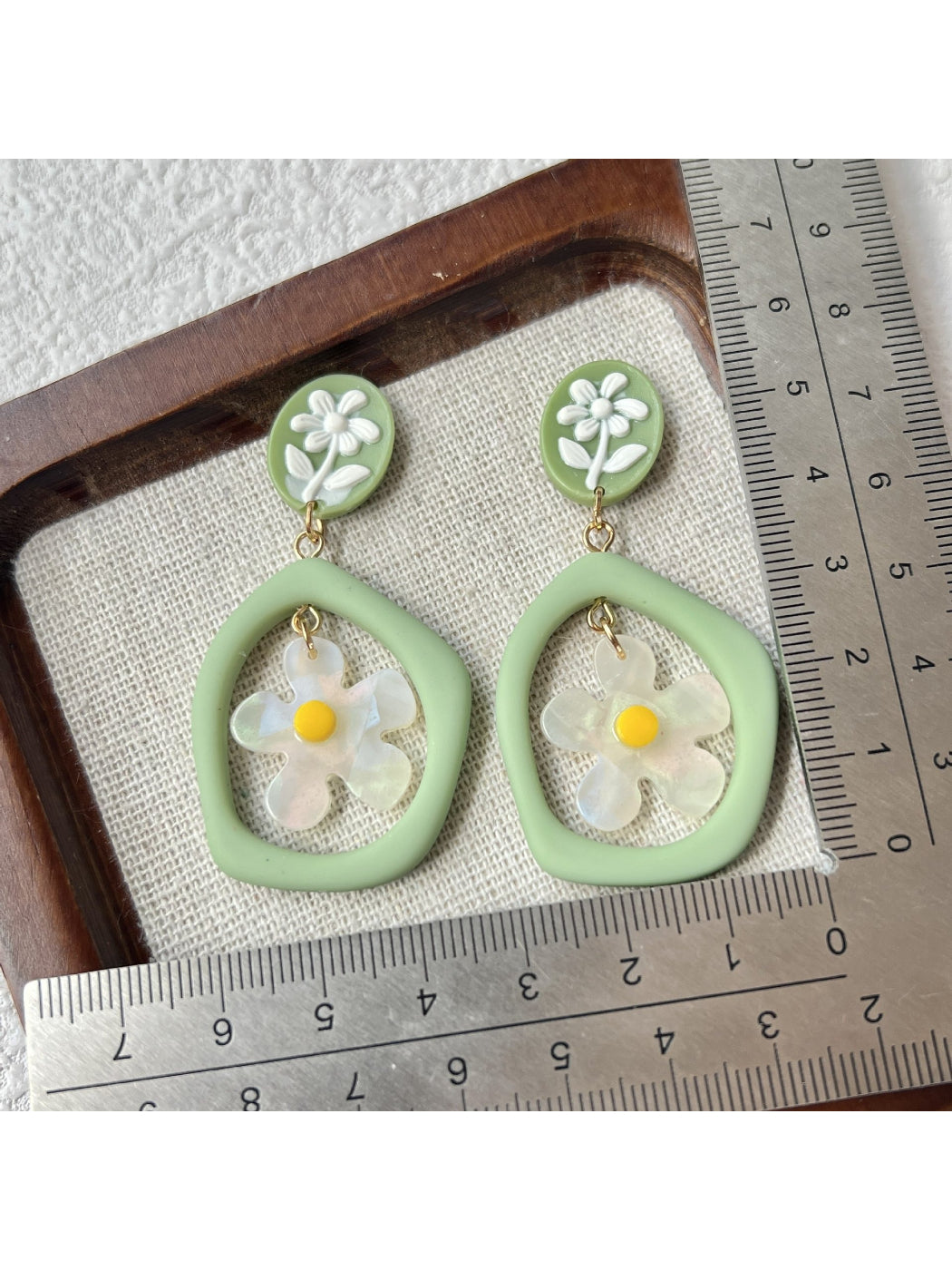 Model wearing green daisy hoop earrings with gold hoops and floral design
