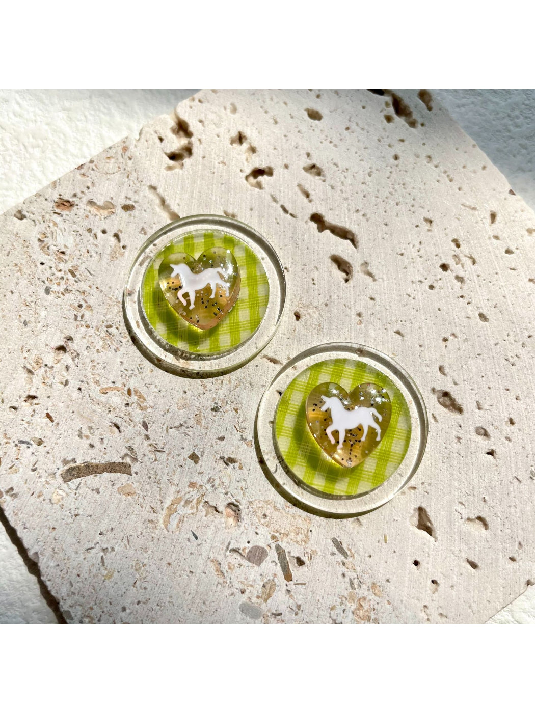 Close-up of green checkered horse-shaped earrings on white background