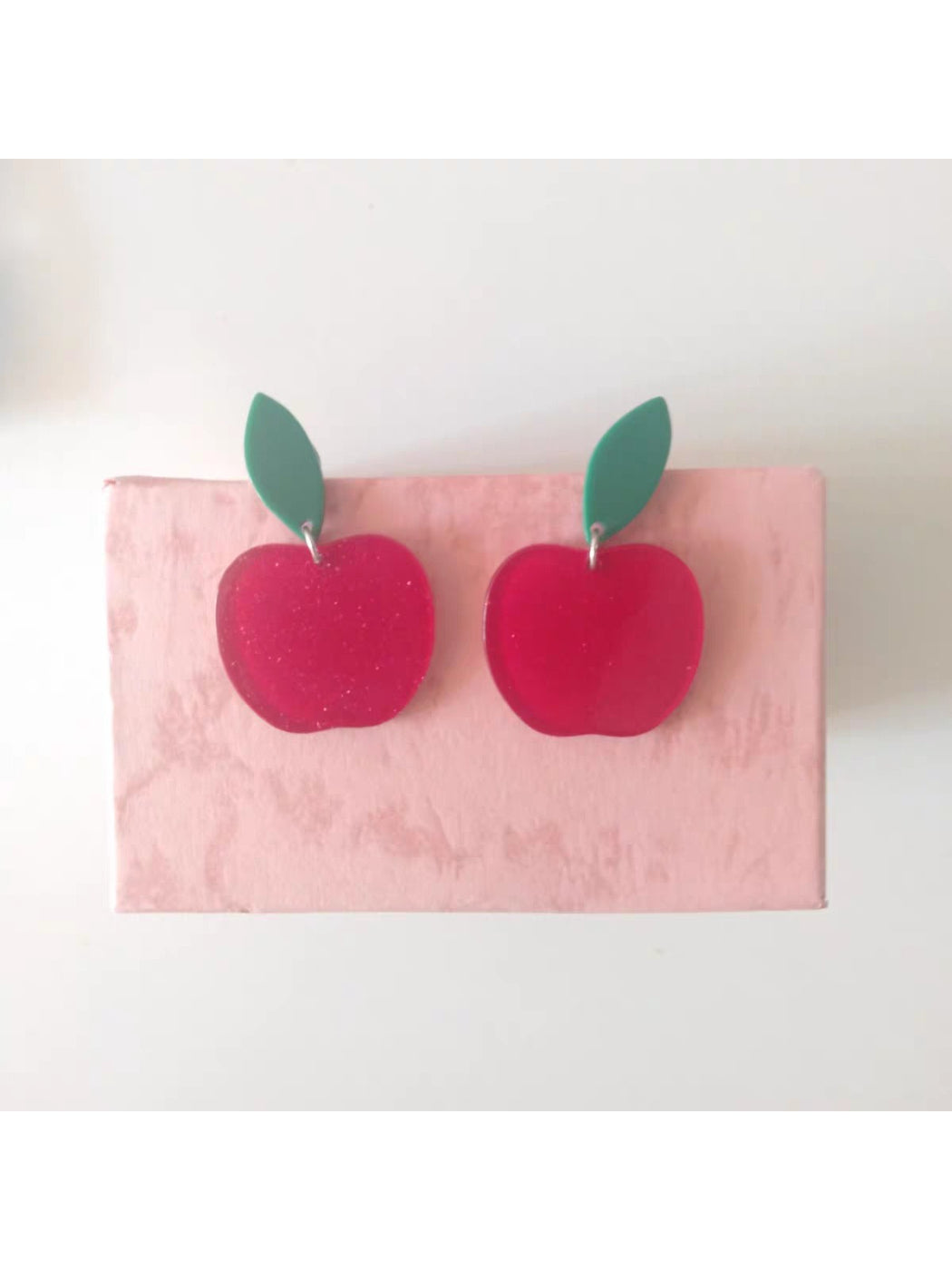 Pair of red apple drop earrings displayed on a wooden surface with green leaves