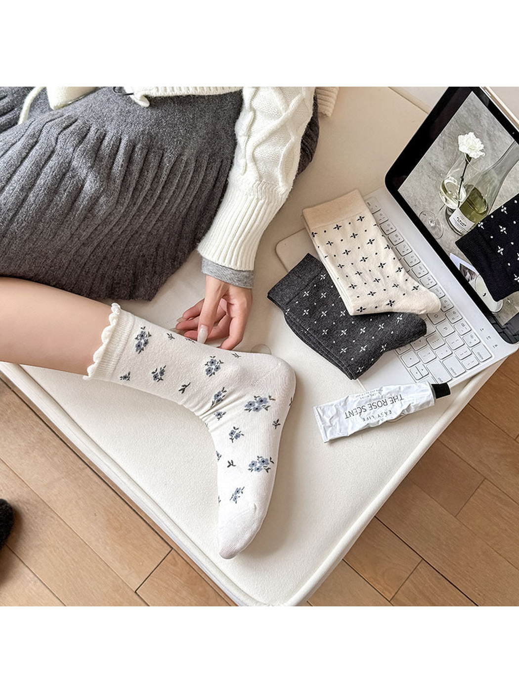White floral sock worn on a foot beside folded socks on a chair