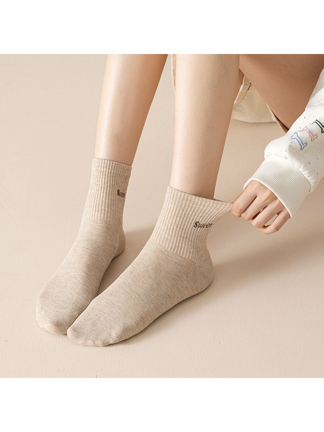 Beige crew socks with lettering worn while adjusting the cuff