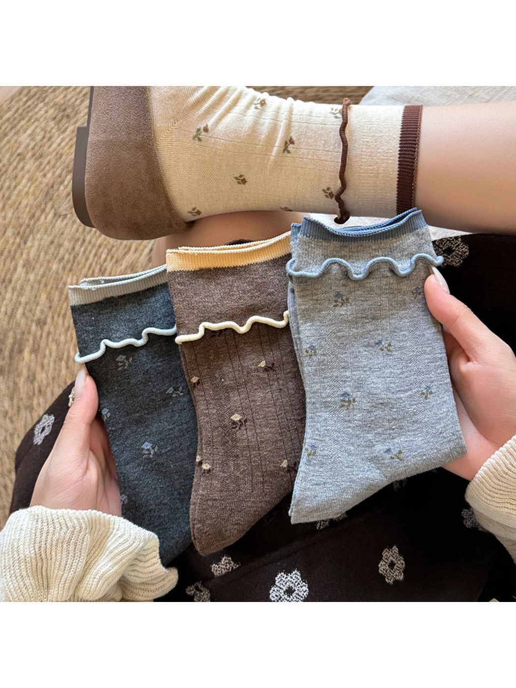 Floral socks held in three colors beside an Ivory sock worn with a brown shoe