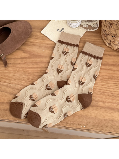 Beige crew socks with pale peach tulip motifs, raised wavy lines, and brown heel and toe panels.