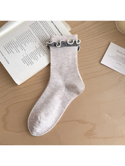 Ivory ribbed sock with contrasting gray ruffled trim below the cuff.