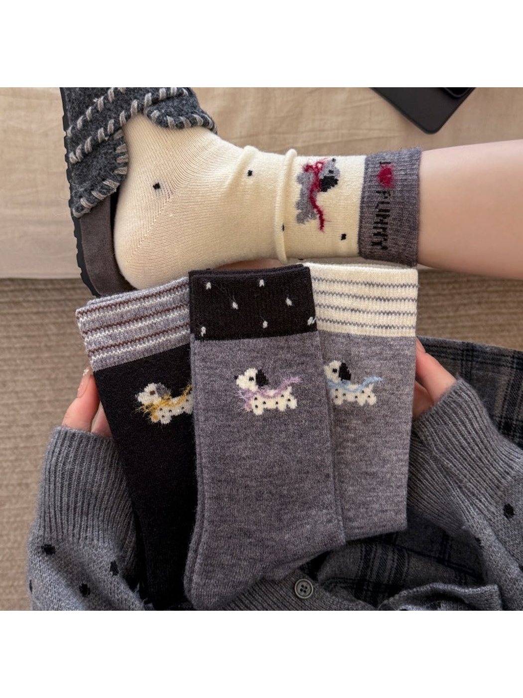 Dog-motif socks with yellow, purple, blue and red scarves, shown folded in hands and worn with a slipper.