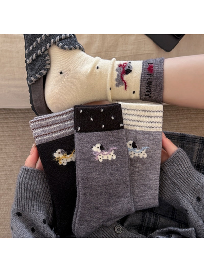 Dog-motif socks with yellow, purple, blue and red scarves, shown folded in hands and worn with a slipper.