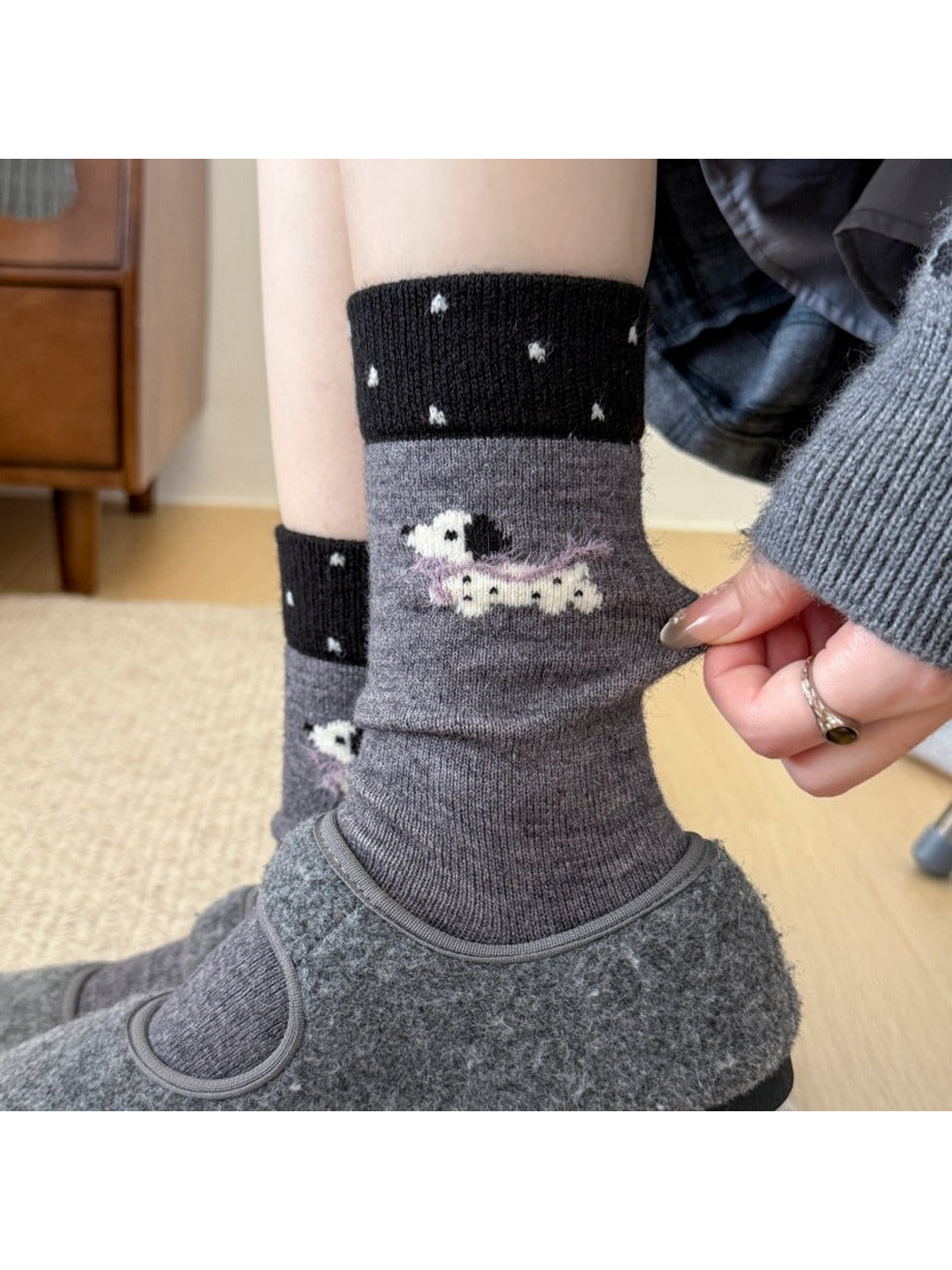 Dark gray socks with dotted black cuffs and a dog with a purple scarf, worn with slippers while the fabric is pulled.