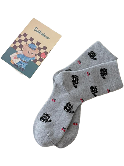 Light gray Cats socks with black cat and red cherry motifs displayed on a cream throw.