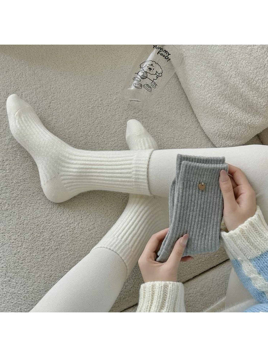 Ivory ribbed socks worn while gray socks are held in both hands.