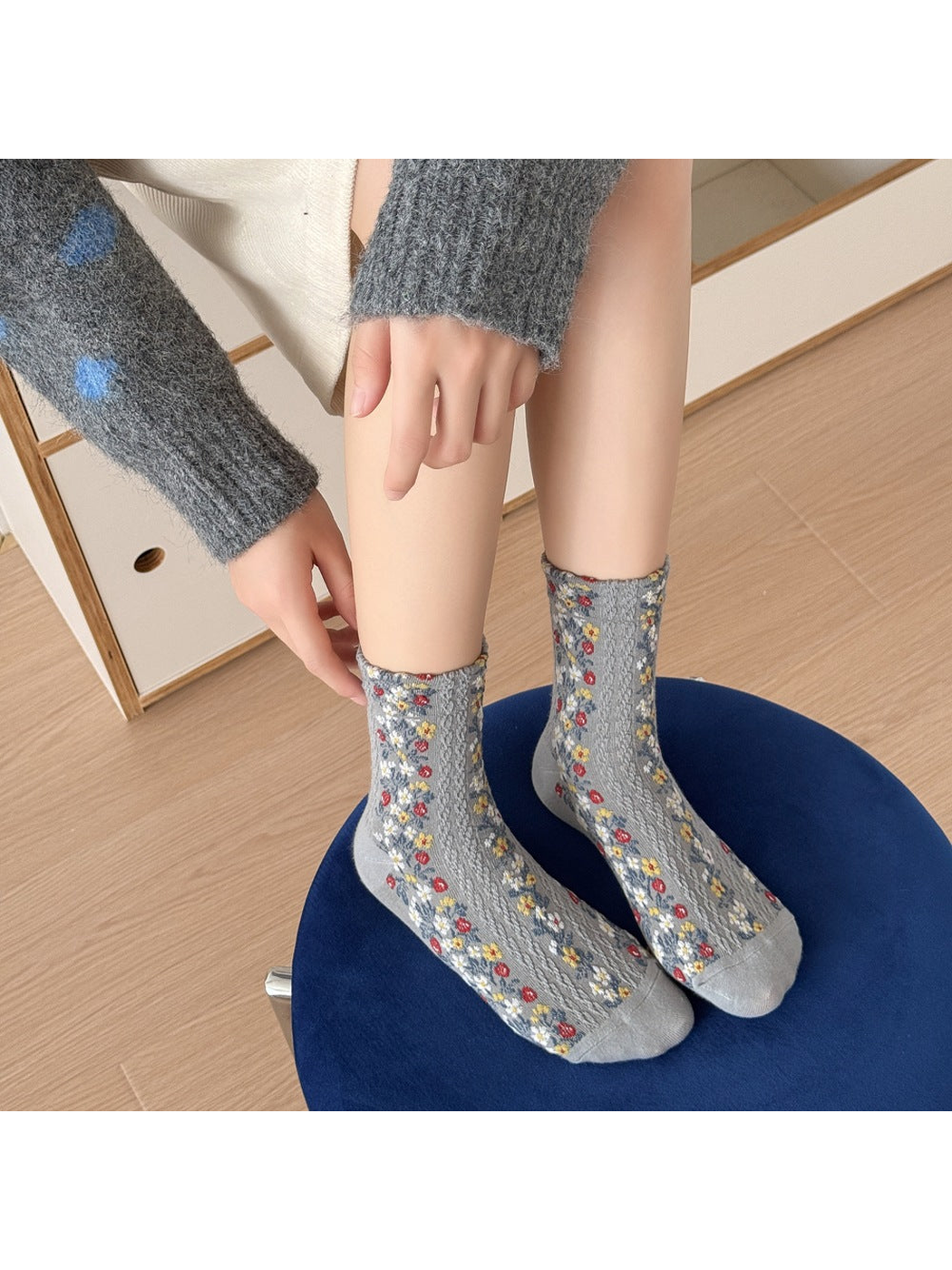 Gray floral socks worn with both feet resting on a blue stool.