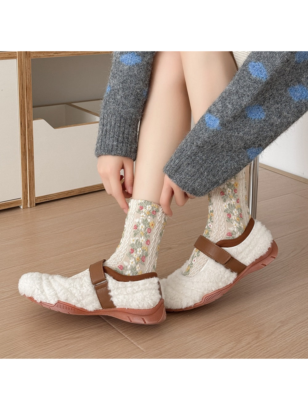 Beige floral socks worn with white shoes with brown straps, with hands adjusting a cuff.