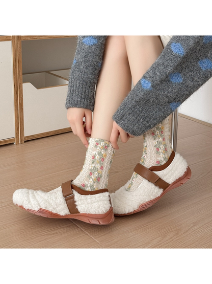Beige floral socks worn with white shoes with brown straps, with hands adjusting a cuff.