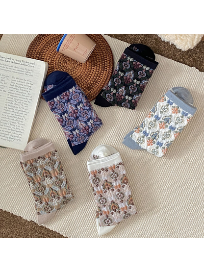 Five colors of folded floral socks arranged on a cream rug.