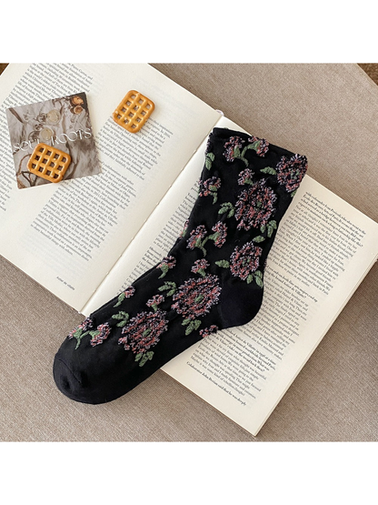 Black sock with raised pink flowers, green leaves and plain toe and heel sections.