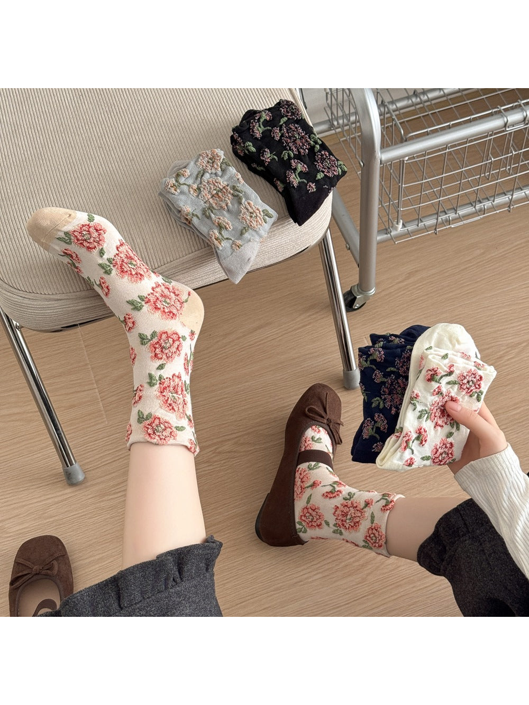 Ivory floral socks worn while holding folded White and Navy socks, with Gray and Black socks on a chair.