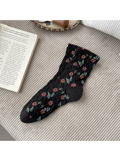 Black socks with pink flowers, green leaves and raised scrolling texture.