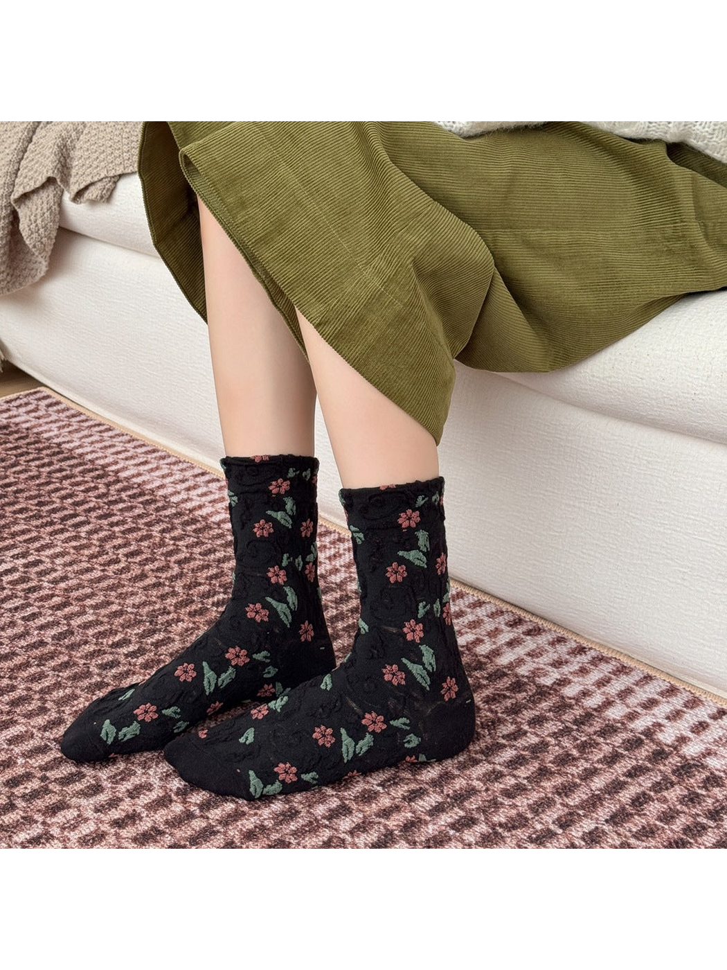 Black floral socks worn with an olive skirt beside a sofa.