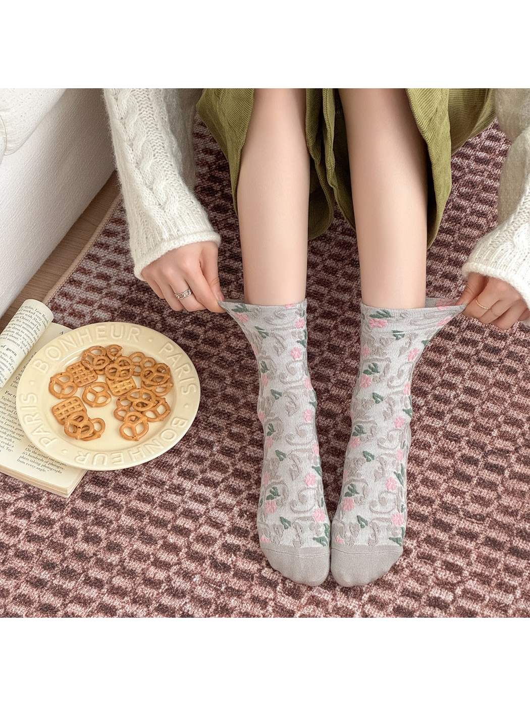 Hands pulling the cuffs of worn Light Gray floral socks outward.